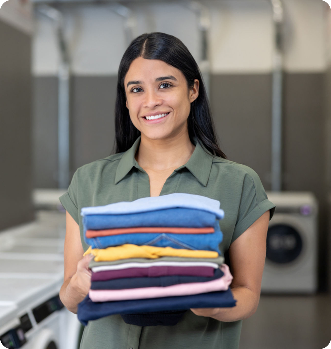 Woman holding folded laundry in laundromat.